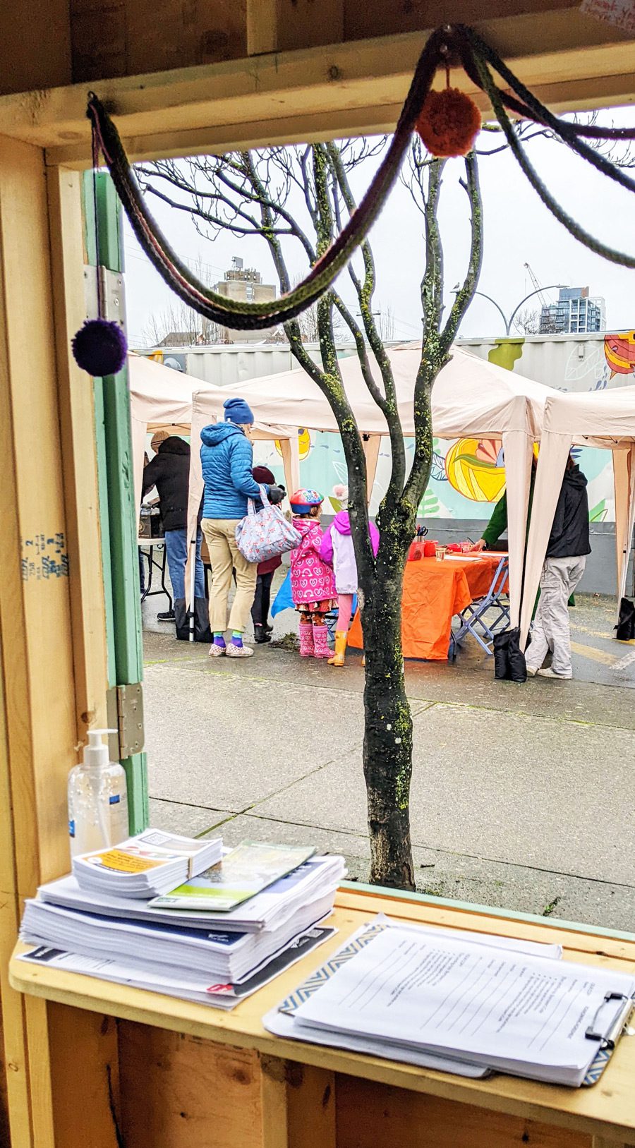 An adult and three kids stop by a market booth on a cloudy day.